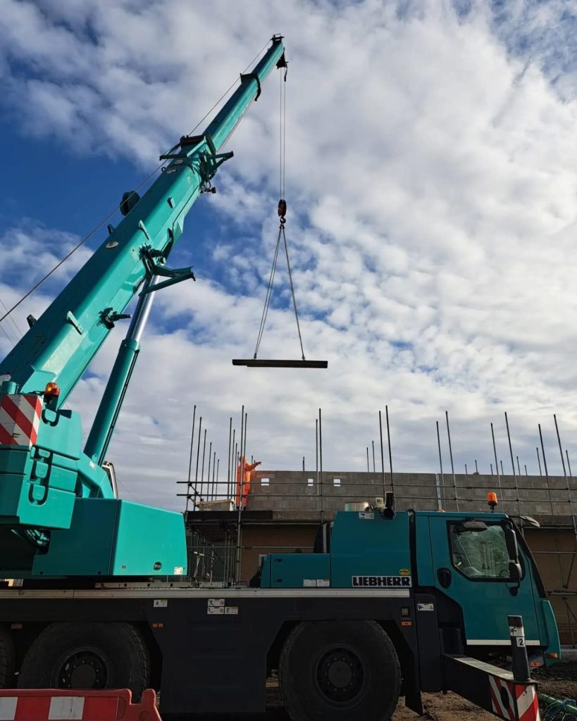 Green crane lifting steel beam on development project