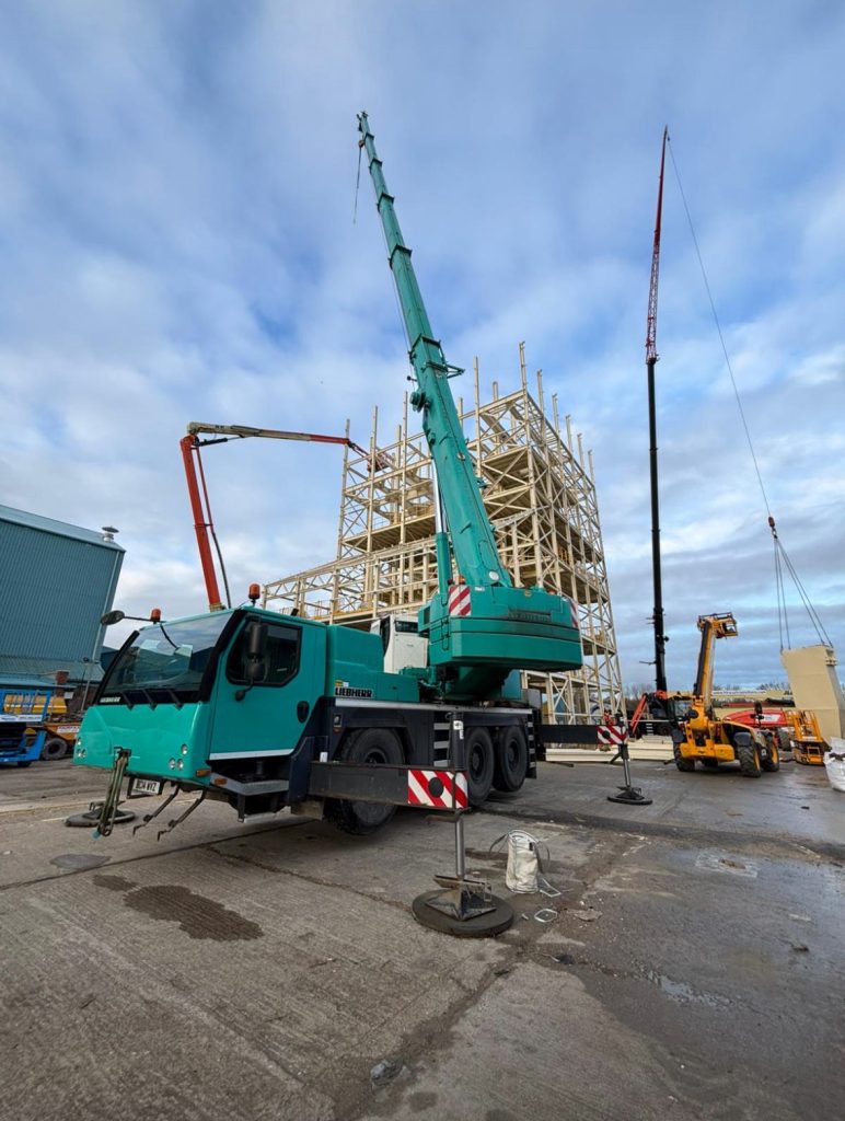 Green crane lifting structural steel on building project
