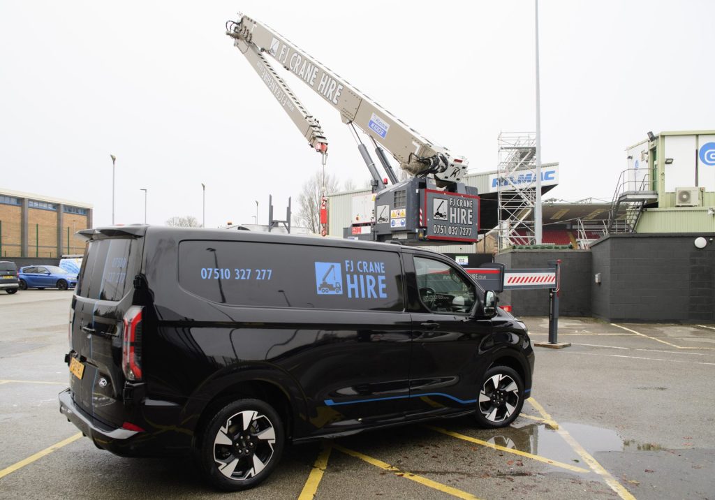 Mobile crane lifting load beside black company vehicle