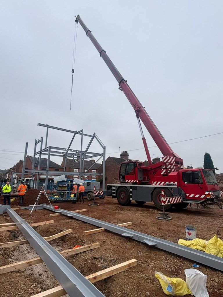 Red mobile crane erecting steel framework on industrial build