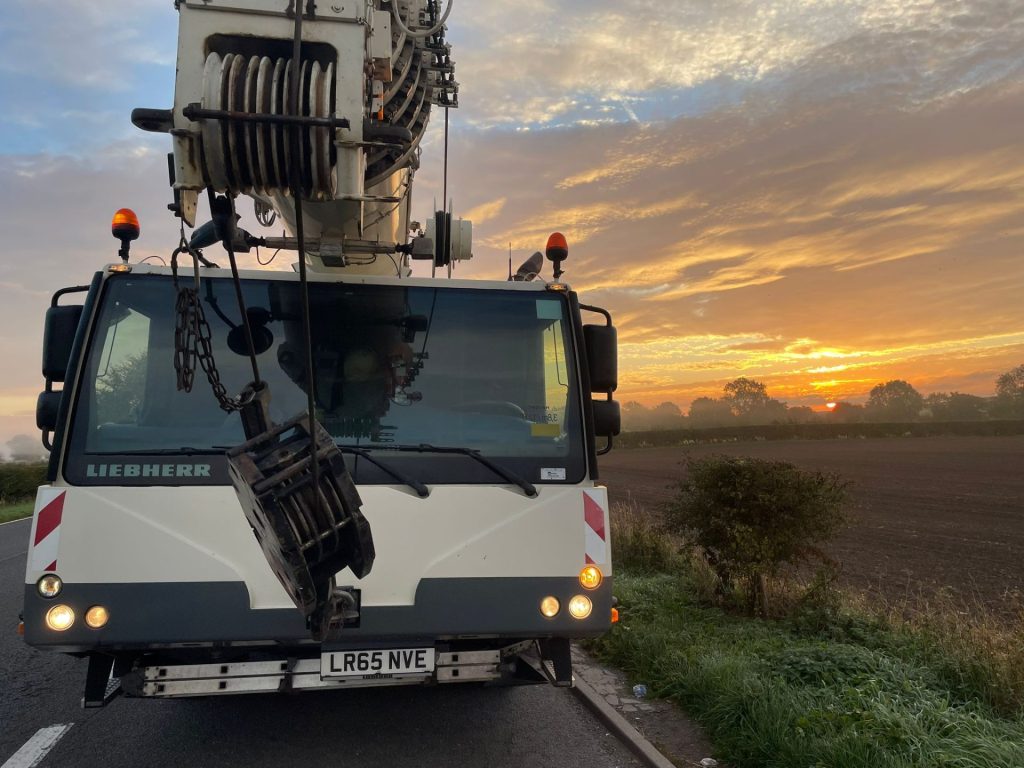 Crane transporting heavy equipment at sunset